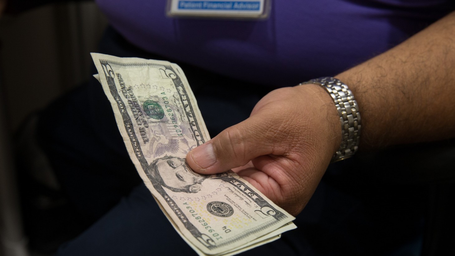 A man's hand holding a five dollar bill 