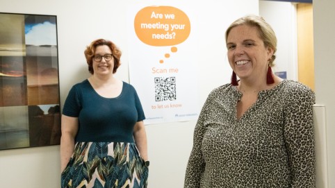 Two women next to wall poster. 