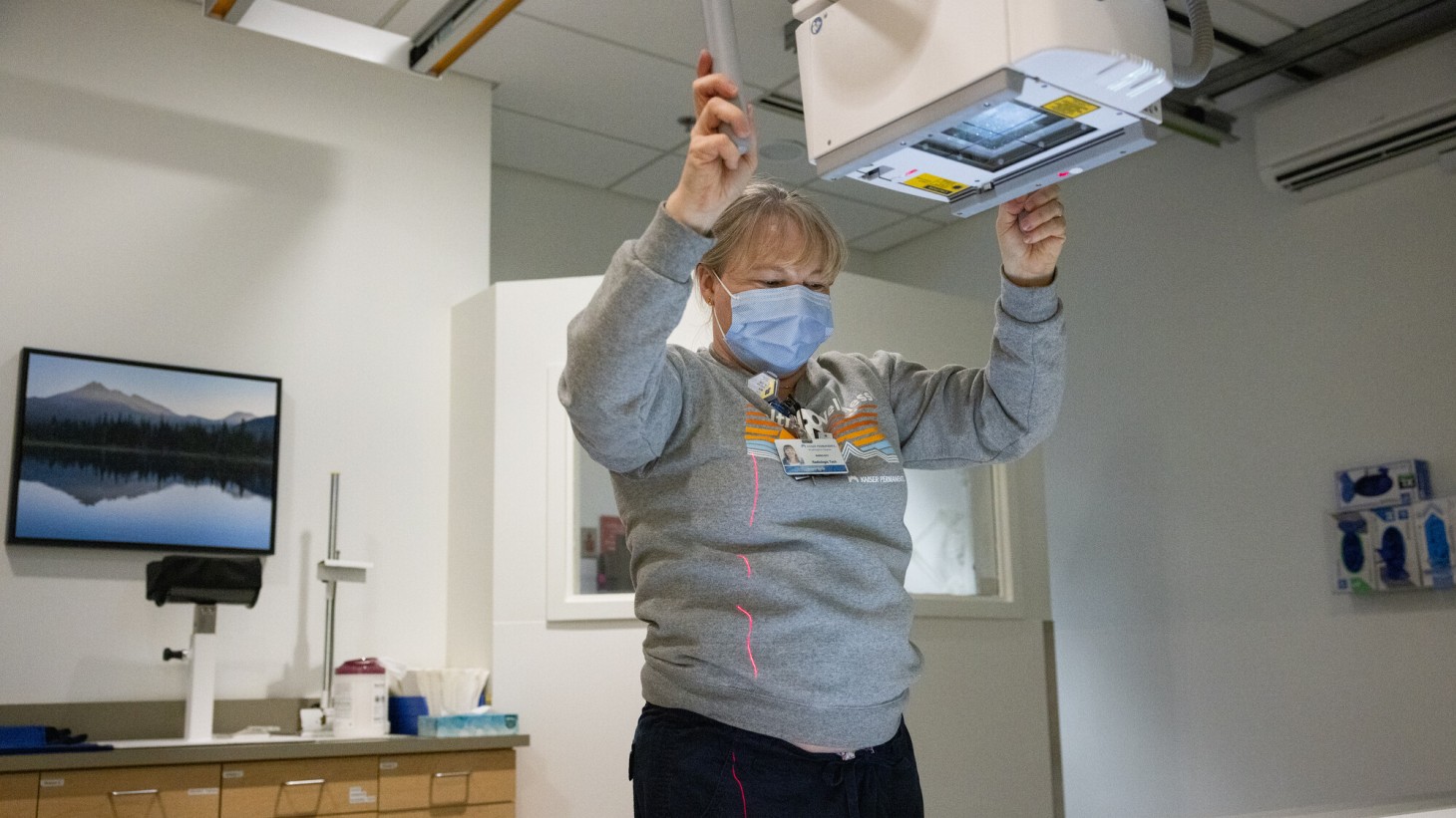 A woman wearing a gray sweatshirt operating an X-ray machine