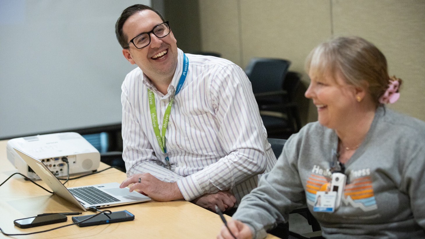 A man and a woman laughing while sitting in chairs at an office table